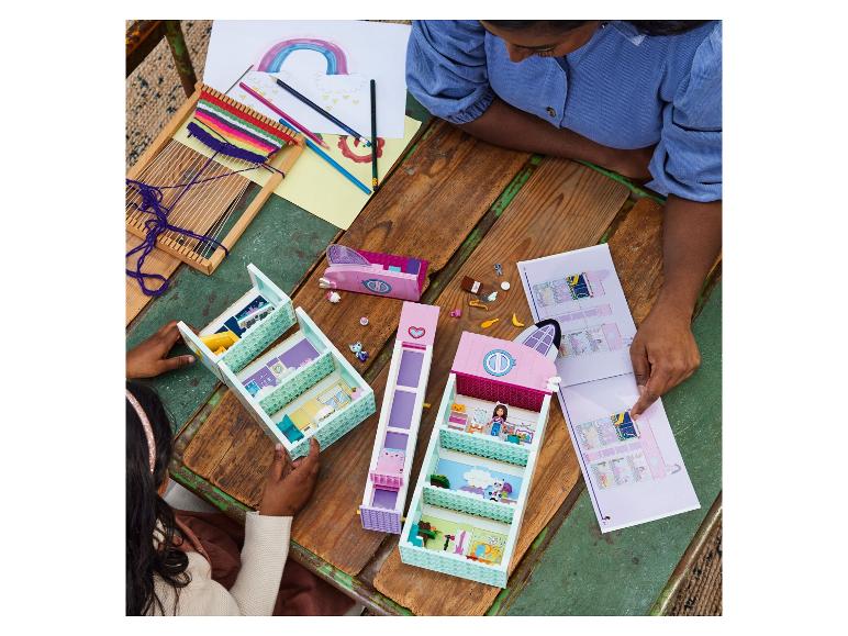 Zwei Mädchen bauen ein LEGO Friends Set auf einem Holztisch mit Zeichnungen und Weberei.