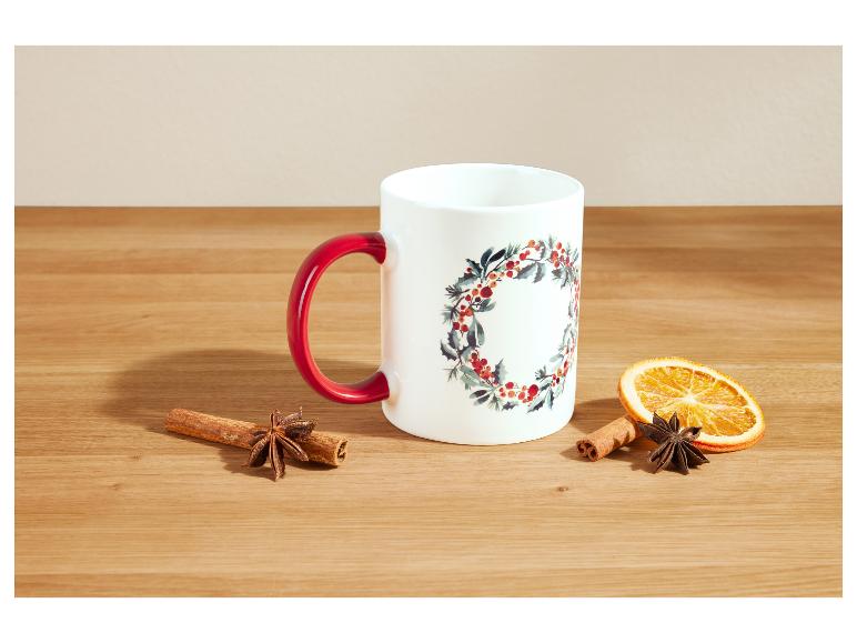 Weiße Tasse mit rotem Henkel und Weihnachtsdekoration, daneben Zimt und Sternanis.