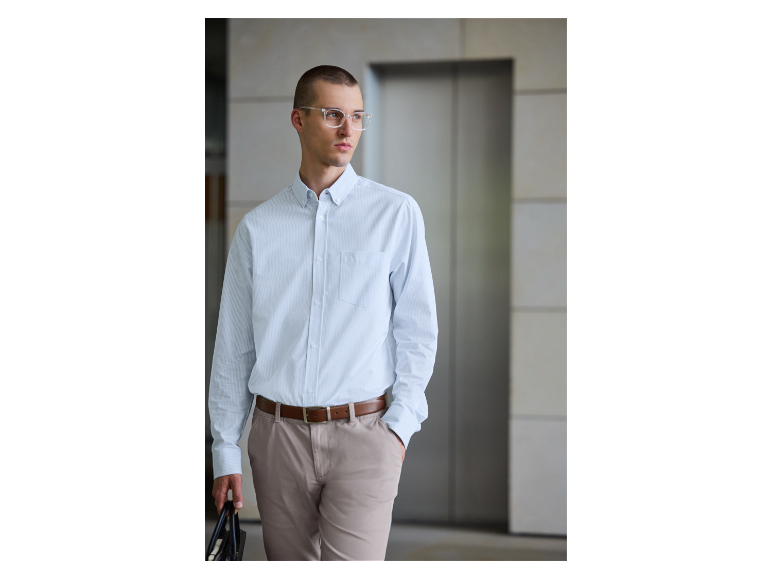 Ein Mann in einem hellblauen gestreiften Hemd und beigen Hosen trägt eine Tasche.