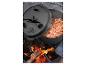 Gusseiserner Dutch Oven mit Chili kocht über offenem Feuer, Deckel teilweise geöffnet.
