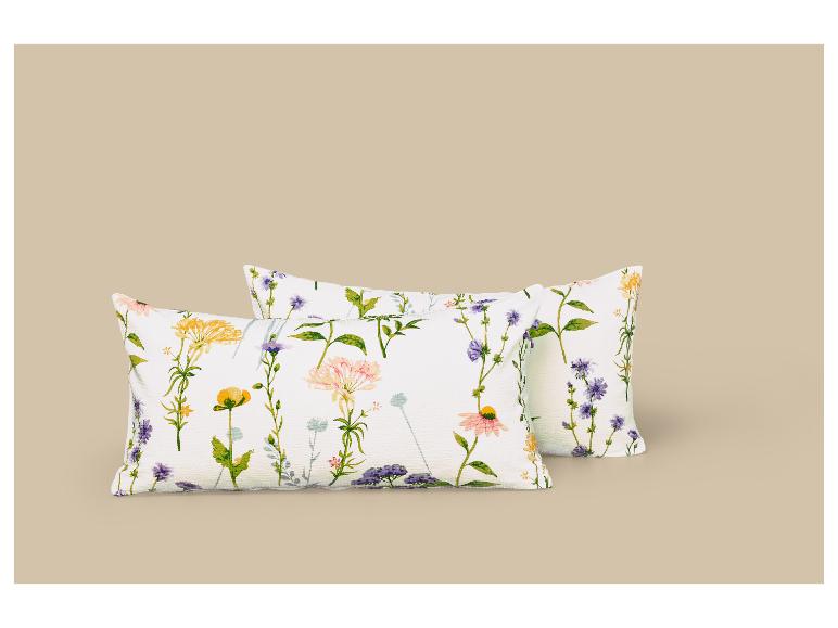 Zwei weiße Kissen mit farbigem Blumenmuster auf beigem Hintergrund.