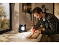 Ein Mann markiert ein Holzbrett auf einer Werkbank, die von einem Akku-LED-Strahler beleuchtet wird.