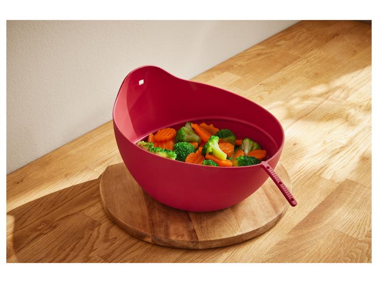 Rote Plastikschüssel mit gekochtem Gemüse auf einer Holzoberfläche.
