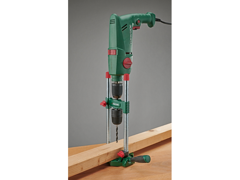 Grüne elektrische Bohrmaschine mit Bohrständer, bohrt in ein Holzbrett.