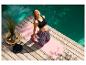 Frau macht Yoga auf rosa Yogamatte an Holzsteg und Pool.