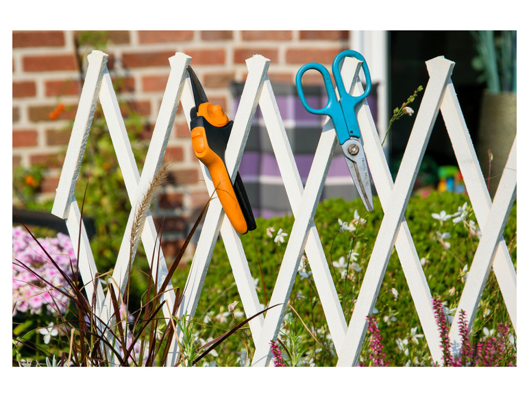 Eine blaue Schere und eine orangefarbene Gartenschere hängen an einem weißen Zaun.