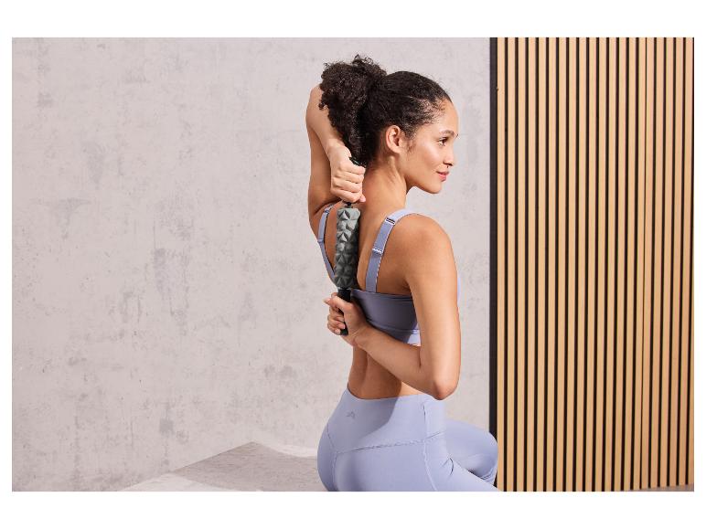 Eine Frau in Sportkleidung verwendet eine Massage-Rolle für ihren Rücken.