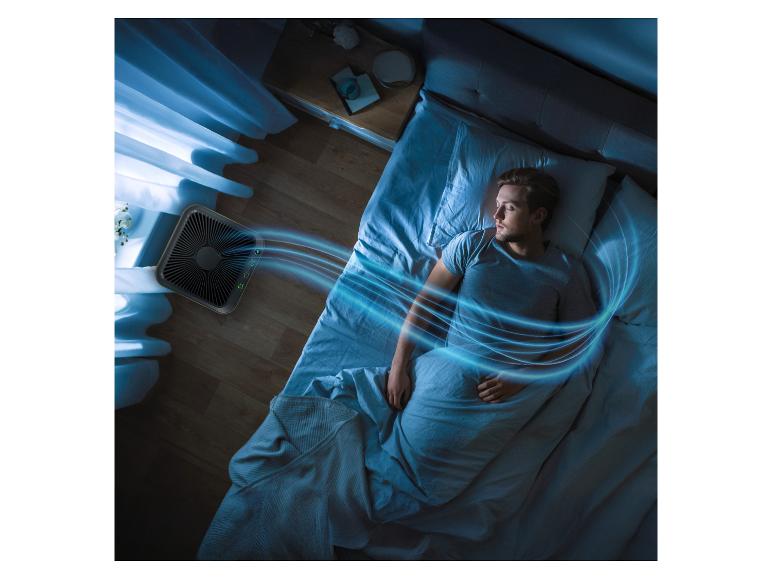 Luftreiniger bläst kühle Luft über schlafenden Mann in dunklem Raum.