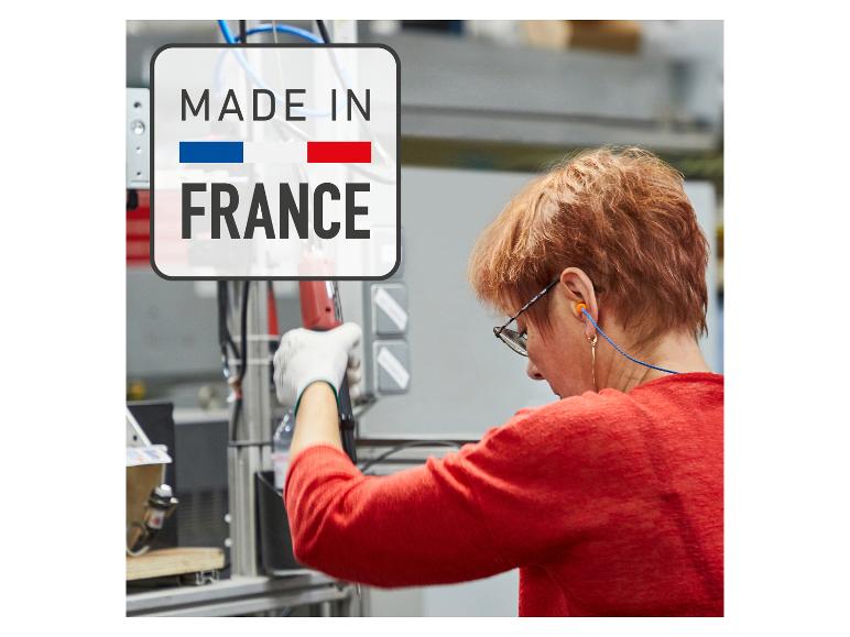 Frau arbeitet in einer Fabrik, mit „Made in France“-Logo im Vordergrund.