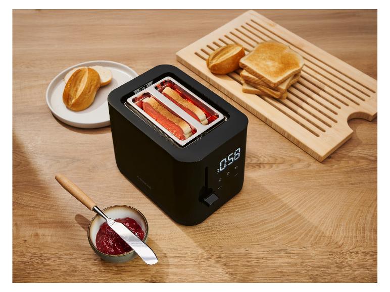 Schwarzer Toaster mit toastendem Brot, Toast, Brötchen und Marmelade auf einem Holztisch.