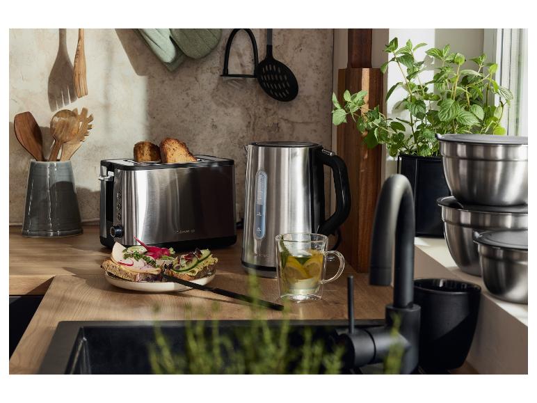 Ein Toaster und ein Wasserkocher aus Edelstahl auf einer Holzarbeitsplatte in der Küche, mit Toast und Tee.