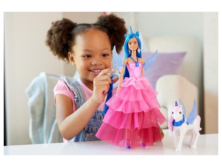 Lächelndes Mädchen spielt mit einer Einhorn-Puppe in einem rosa Kleid und einem Einhorn-Spielzeug.