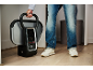 Person hält einen tragbaren Dampfglätter mit Digitalanzeige, trägt Jeans und Turnschuhe.
