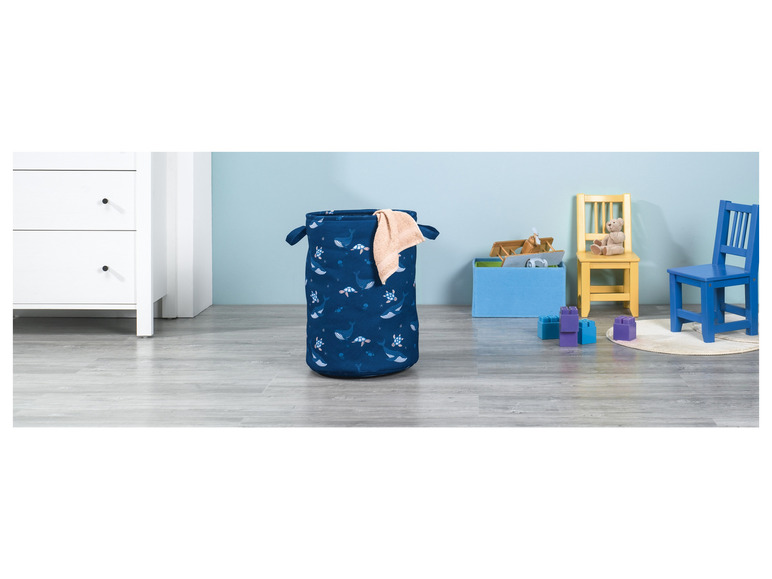 Ein blauer Wäschekorb mit Walen und Schildkröten, zwei Stühle und Bausteine in einem Kinderzimmer.