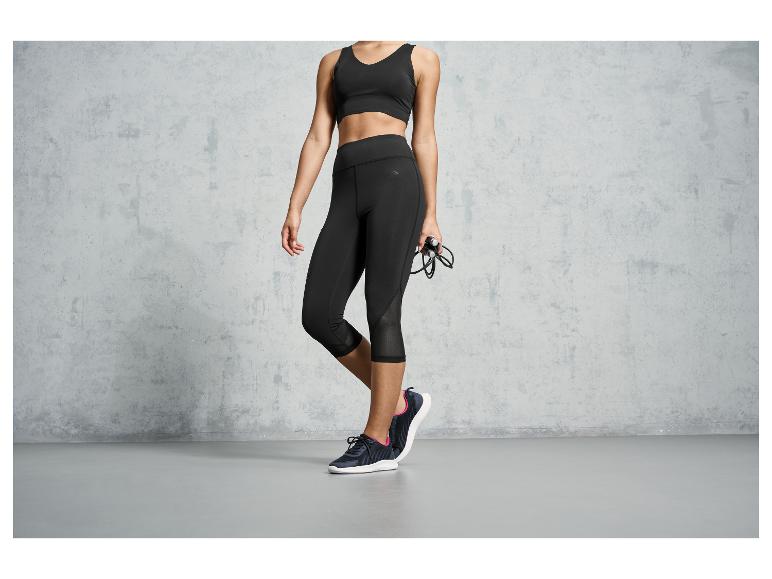 Eine Frau in schwarzen Leggings, einem Sport-BH und Sportschuhen hält ein Springseil.