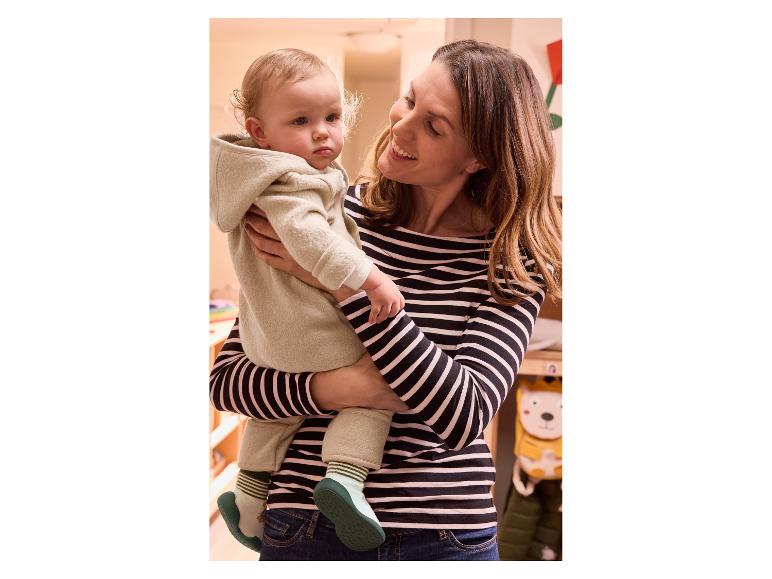 Eine Mutter hält ein Baby in einem hellbeigen Strampler.