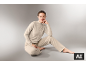 Eine Frau in einem beigen Loungewear-Set sitzt auf grauem Hintergrund
