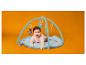 Lächelndes Baby auf einer Spielmatte mit hängendem Spielzeug, orangefarbener Hintergrund.