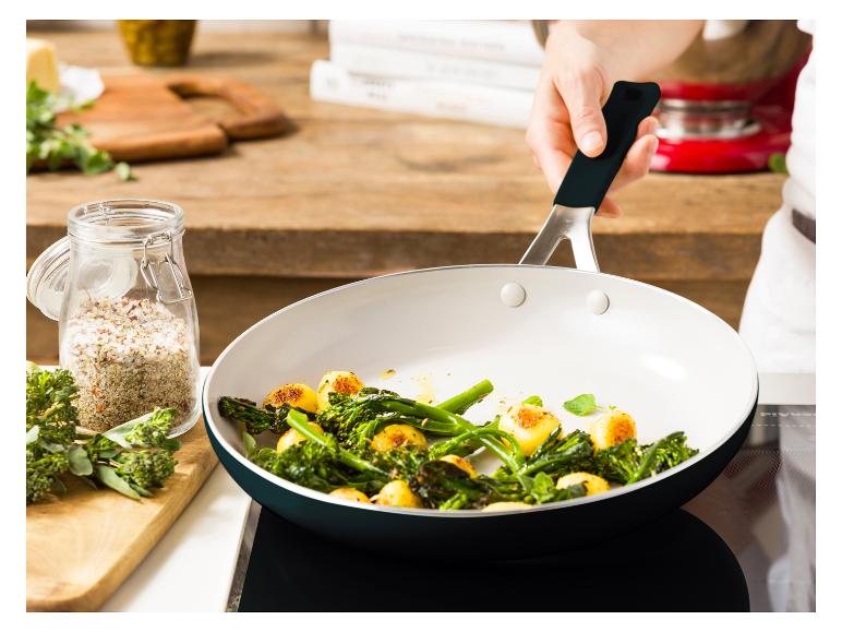 Eine Person kocht Brokkoli und Kartoffeln in einer Pfanne auf einem Kochfeld.