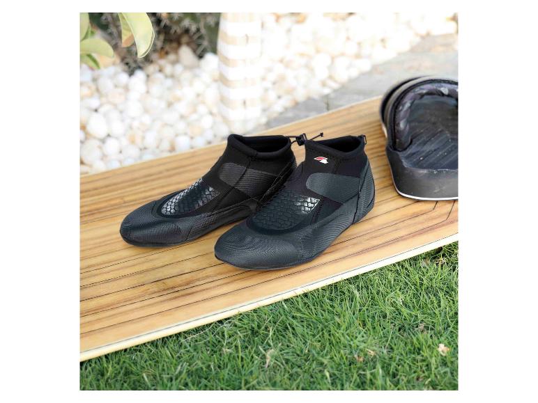 Schwarze Neoprenschuhe auf einem Holz-Surfbrett mit Gras im Hintergrund.