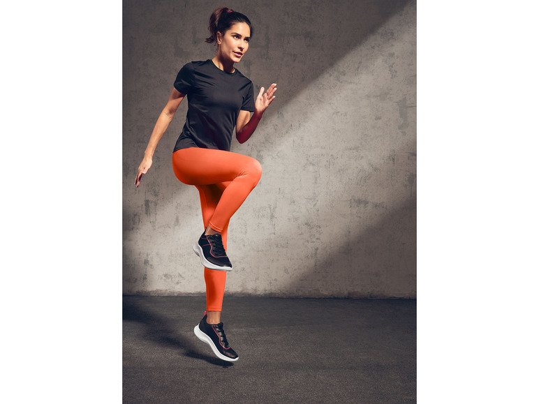 Eine Frau in einem schwarzen Top und orangefarbenen Leggings während einer Trainingseinheit.