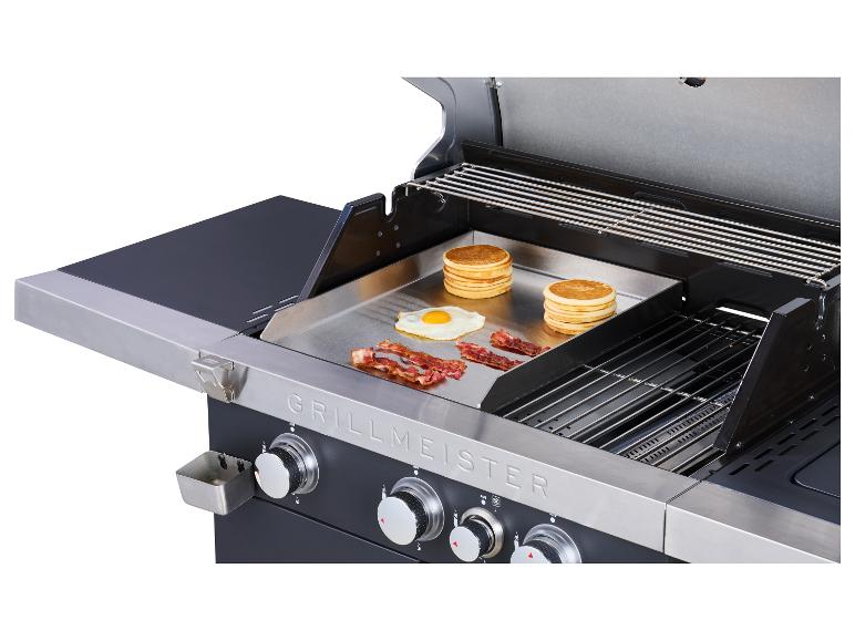 Grill mit Grillplatte, auf der Pfannkuchen, Eier und Speck zubereitet werden.