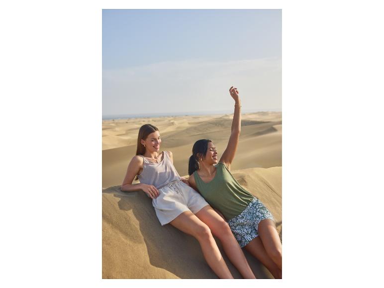 Zwei Frauen in Tanktops und Shorts entspannen sich auf Sanddünen.
