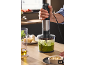 Ein Stabmixer mit Zerkleinerer bereitet grünes Pesto auf einer Küchenarbeitsplatte zu.