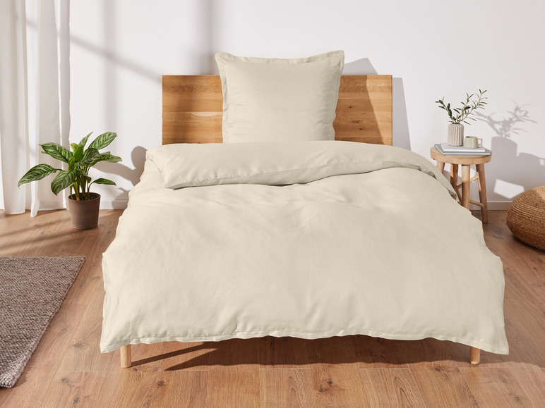 Beige Bettdecke und Kissenbezüge auf einem Holzbett.