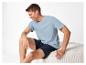 Lächelnder Mann in hellblauem T-Shirt und dunkelblauen Shorts, sitzt auf einem Hocker.
