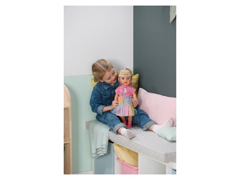 Mädchen in Jeanskleidung spielt mit einer Puppe in einem rosa Kleid auf einer Bank.