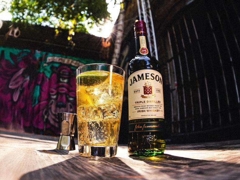 Whiskyflasche und Glas mit Eis und Limette auf Holzoberfläche mit Graffiti-Hintergrund.