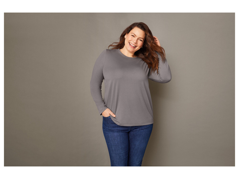 Eine Frau trägt ein graues Langarmshirt und blaue Jeans.