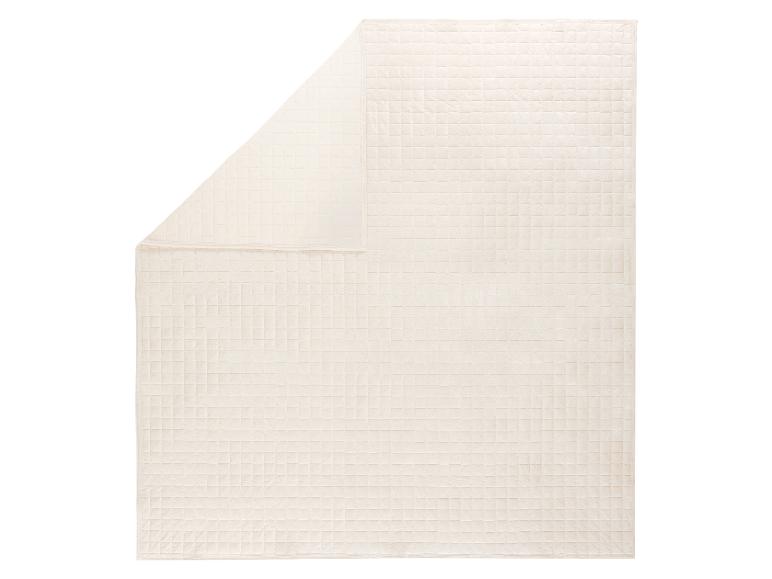 Cremefarbene gesteppte Decke mit Karomuster, teilweise gefaltet.