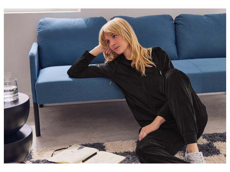 Frau in schwarzem Velours-Trainingsanzug sitzt auf dem Boden mit Notizbuch.
