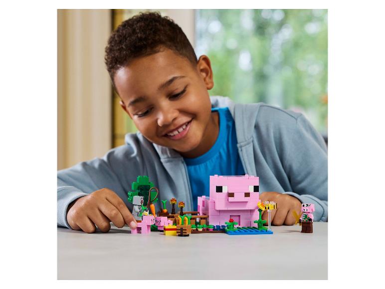 Ein lächelnder Junge spielt mit einem LEGO Minecraft Schweinefarm-Set.