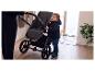 Kind in Winterjacke hält Kinderwagen, schaut zu einem Erwachsenen auf.