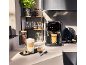 Kaffeemaschine mit zwei Tassen Kaffee, Kaffeebohnen und einer Pflanze in der Küche.