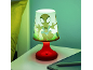 Tischlampe mit Zeichentrickfigur und rotem Sockel, neben einem Bett.