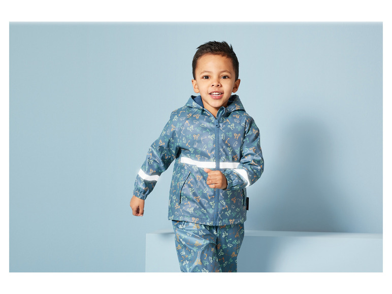 Ein Junge trägt einen blauen Regenmantel und eine Hose mit Fahrradmuster.
