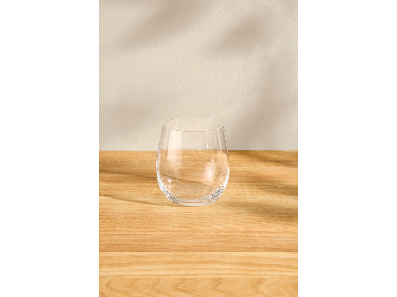 Leeres klares Glas auf einem hellen Holztisch mit zarten Schatten an der Wand.