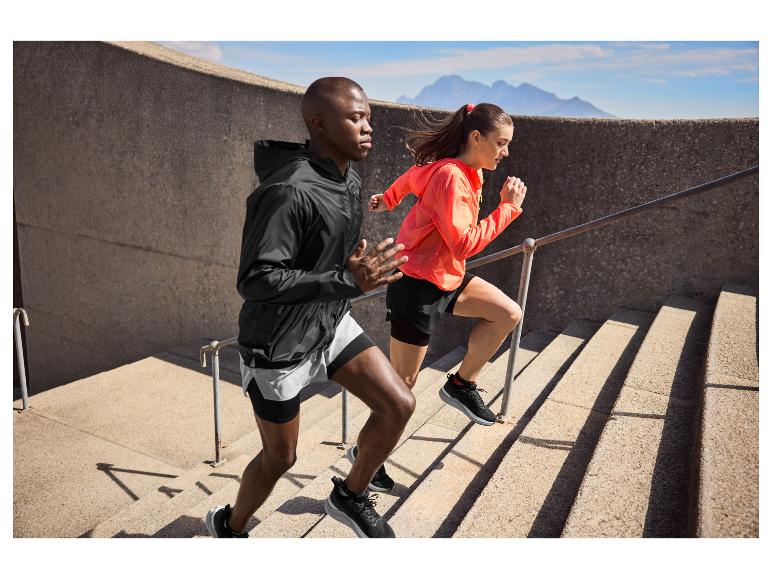 Zwei Sportler in Sportkleidung laufen Außentreppen hoch mit Bergen im Hintergrund.