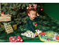 Ein Kleinkind im festlichen Schlafanzug sitzt neben einem Weihnachtsbaum mit Geschenken und einem Grinch-Kissen.