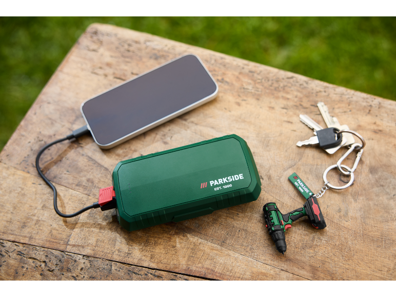 Grüne Powerbank lädt ein Smartphone, mit Schlüsseln und Mini-Bohrmaschinen-Schlüsselanhänger.