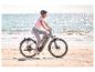 Frau auf einem E-Bike am Strand, mit glitzerndem Meer im Hintergrund.