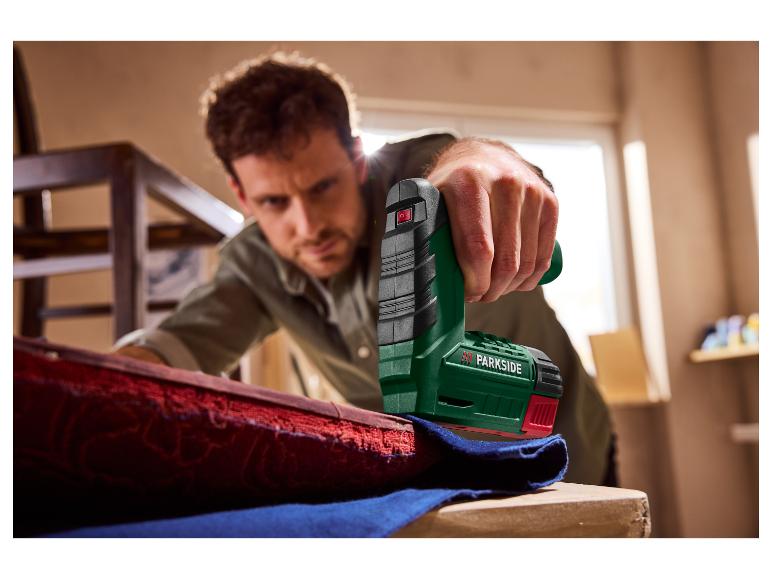 Mann benutzt PARKSIDE® 4V Akku-Tacker PAT 4 D6 zum Befestigen von rotem Stoff.
