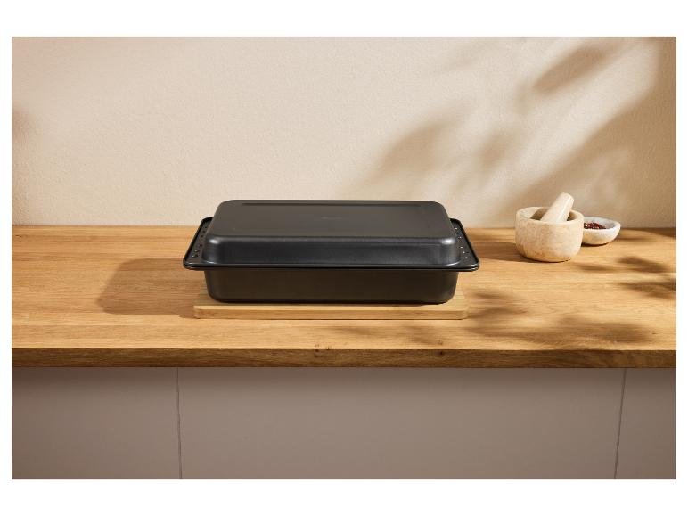 Schwarze Auflaufform mit Deckel auf einem Holztisch, mit Mörser und Gewürzen.