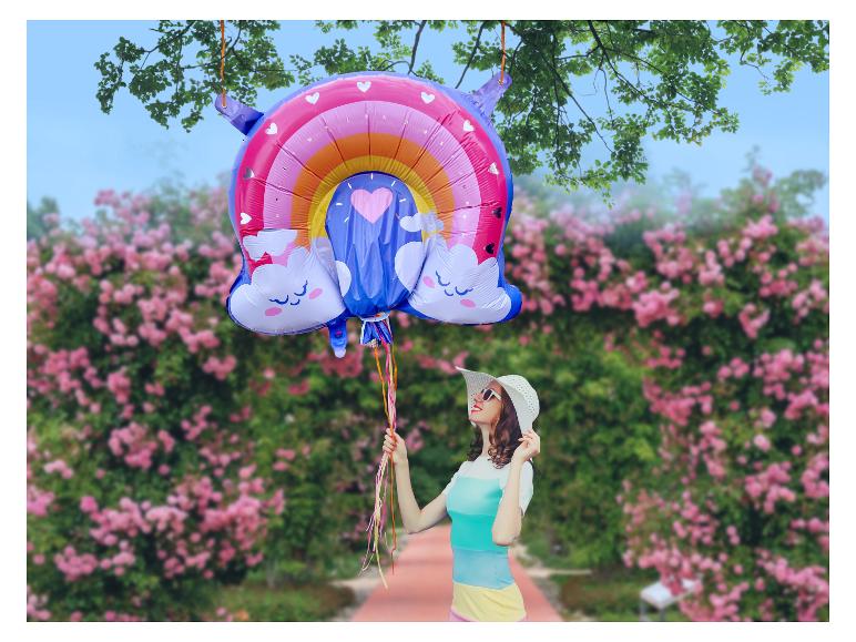 Frau mit Hut und Regenbogenballon in einem Rosengarten.