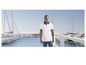 Ein Mann in einem weißen Poloshirt und blauen Jeans steht vor einem Yachthafen.