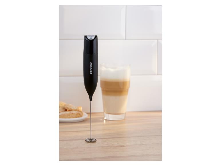 Schwarzer Milchaufschäumer auf Holzoberfläche neben einem Glas Latte und Keksen